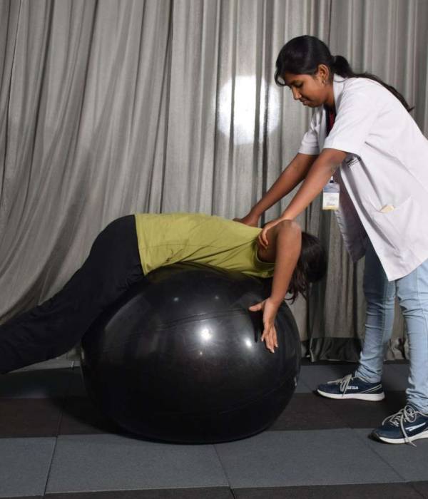 A woman lying on a black ball with a physiotherapist helping her