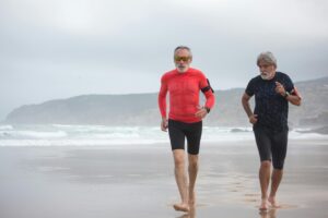 Two senior men run together on the beach