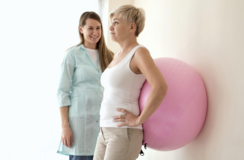 A woman stands beside another woman holding a pink ball, both smiling and enjoying their time together.