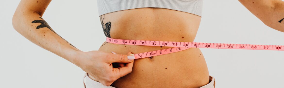 A woman measuring her waist with a pink tape measure, focused on her fitness goals.