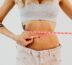A woman measuring her waist with a pink tape measure, focused on her fitness goals.